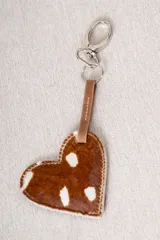 Llavero en forma de corazón confeccionado en cuero con pelo estampado tipo animal print, con tira de cuero lisa y gancho metálico.