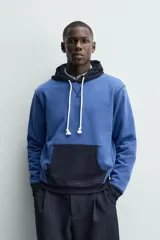 Sudadera hoodie regular fit de color azul, con capucha y bolsillo canguro negro. Cuenta con cordones ajustables blancos y detalles en color negro en la capucha, el bolsillo y los puños.