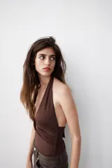 Body de cuello halter confeccionado en mezcla de poliamida, con abertura frontal y aplicación metálica forrada. Presenta diseño drapeado en los laterales, espalda descubierta y cierre inferior con botones a presión.
