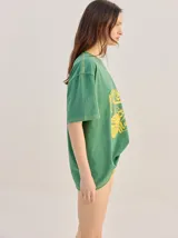 Remera oversize de corte cuadrado, color verde, con cuello redondo y estampa retro centrada en tono amarillo.