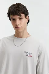 Remera de manga corta color gris claro, con cuello redondo y estampado pequeño en el pecho con texto en rojo y negro.