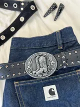 Cinturón negro de cuero sintético con hebilla plateada con diseño de botas cowboy.