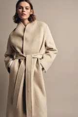Abrigo largo de corte minimalista confeccionado en mezcla de lana, con diseño de solapas integradas, manga larga y cinturón ajustable del mismo tejido.