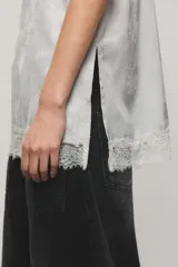 Top negro de satén jacquard, con escote en V de estilo lencero decorado con puntilla delicada al igual que el ruedo, breteles finos regulables y aberturas laterales.