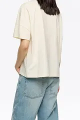 Camiseta de manga corta, corte oversize, color marrón oscuro. Presenta un estampado frontal con el texto "BIMBA Y LOLA" realizado con hilos de colores vibrantes que cuelgan, simulando un bordado texturizado.