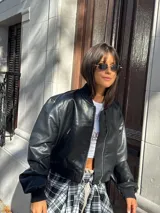 Campera estilo bomber de cuero sintético en color negro, con cierre frontal, cuello, puños y ruedo acanalados. Presenta un diseño corto y holgado.
