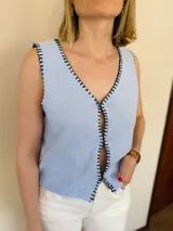 Chaleco tejido color arena con terminaciones en punto festón negro.