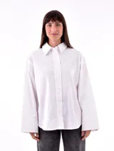 Camisa blanca de corte amplio, con cuello clásico y mangas largas con puños abotonados.