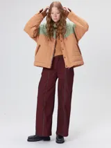 Campera acolchada de diseño colorblock, con el pecho y hombros en tono bordó y el cuerpo y mangas en color beige. Presenta cuello camisero y puños de pana negra, cierre frontal oculto con botones a presión y costuras pespuntadas en patrón cuadriculado.