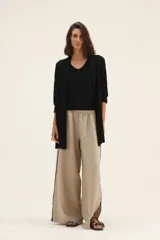 Pantalón de lino color beige, de corte ancho, con cintura elástica y ribete negro en los laterales con tajos en el ruedo.