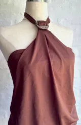 Vestido corto marrón oscuro, estilo halter con cuello anudado en una argolla central. Presenta un diseño drapeado en la parte superior que cae sobre una falda ajustada.