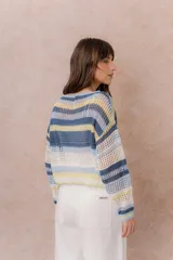 Buzo tejido de punto calado con rayas horizontales multicolor en tonos azul, amarillo, celeste y blanco, con escote bote, mangas largas y hombros caídos. Incluye top básico al tono.