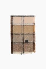 Pashmina de tejido suave con diseño de cuadros en tonos beige, marrón y negro. Presenta bordes desflecados y una etiqueta decorativa pequeña en color negro.