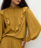 Blusa Marfinno de manga larga color mostaza, con cuello padre y acabado liso con panel delantero texturizado. Presenta volados aplicados en el busto.