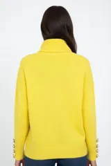 Polerón de cuello alto en color amarillo, con mangas largas y detalle de botones decorativos en los puños.