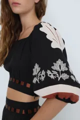 Top corto negro con escote bardot, mangas cortas abullonadas con bordado floral blanco y detalle de recortes con tiras horizontales color café en la cintura.