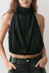 Blusa negra de gasa con escote halter y diseño drapeado frontal. Presenta un corte holgado con elástico en la cintura y espalda descubierta.