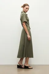 Maxi vestido camisero verde oliva, de manga corta, cuello camisero, cierre frontal con botones, bolsillos con solapa en el pecho, bolsillos laterales y lazo ajustable en la cintura.