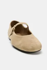 Zapato tipo bailarina de ante color beige, con punta redonda, suela plana de 1 cm y tira delantera con hebilla metálica.