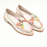Mocasín de cuero color off-white vainilla, con taco bajo, punta redondeada y detalles artesanales de tiras entrelazadas en tonos pastel y aplique colgante con cuenta translúcida en el empeine.