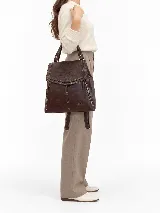 Mochila de cuero vacuno marrón con acabado pulido, solapa en forma de V y costuras decorativas. Cuenta con cremalleras laterales y asas ajustables.