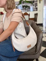 Cartera tipo hobo de cuero color crudo con correa de cuero marrón.