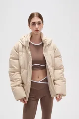 Campera puffer color beige con diseño capitoneado, capucha integrada y cierre frontal oculto. Presenta bolsillos laterales y un corte holgado.