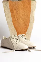 Zapatillas bajas color crema con cordones y suela marrón.