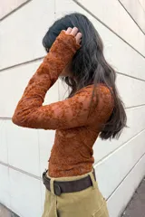 Top de manga larga color marrón óxido, confeccionado en tejido de encaje floral. Presenta escote en V con cierre frontal de botones pequeños.