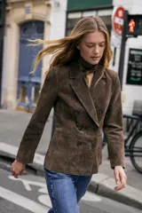 Blazer cruzado de mujer, color marrón oscuro, confeccionado en piel 100%. Presenta cuello solapa, manga larga con hombreras, bolsillos delanteros de doble vivo y cierre frontal cruzado con botones oscuros.