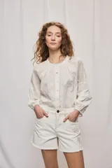Short de denim blanco de calce recto y tiro medio, con bolsillos delanteros, cierre con botón y terminación desflecada en el ruedo. Presenta detalles florales bordados al tono en el frente.