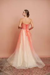 Vestido largo de fiesta, strapless, con busto drapeado y falda de tul con degradé de color coral a blanco. Presenta bordados florales en el corpiño.