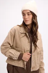 Campera de denim en tono beige, de corte cropped, con cuello camisero, cierre frontal con botones metálicos y bolsillos frontales tipo parche.