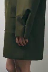 Cazadora impermeable de acabado engomado en color amarillo, con capucha ajustable, cierre frontal con botones a presión, bolsillos laterales y mangas largas ajustables.