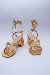 Sandalias doradas con taco cuadrado y tiras finas que se atan al tobillo. Capellada, forro y plantilla 100% de cuero.