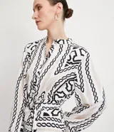 Vestido midi estilo chemise de satén con estampado de cadenas en blanco y negro. Tiene cuello redondo, mangas largas con puños elásticos, abotonadura frontal y cinturón con hebilla redonda.