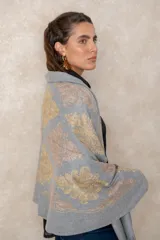 Pashmina de tela densa y suave, con caída pesada y diseño bordado con motivos florales en tonos dorados y beige. Presenta terminaciones con flecos en los extremos.