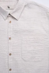 Camisa de manga corta color crema con textura, botones de madera y parche con logo.