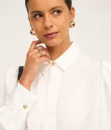 Camisa de crepé color blanco, con cuello inglés, manga larga abullonada con puños abotonados y cierre frontal oculto con botón diferenciado en el cuello.
