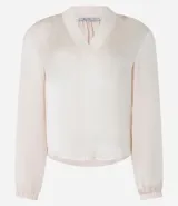 Blusa de manga larga color crema o blanco roto, con textura satinada y escote en V con cuello solapa. Las mangas terminan en puños elásticos.