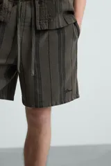 Bermuda de algodón color blanco, de corte relajado (relaxed fit), con cintura elástica ajustable mediante cordón. Posee bolsillos laterales y un bolsillo trasero de plastrón. Presenta un bordado en contraste en la pernera.