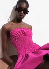 Vestido corto fucsia de estilo palabra de honor con cuerpo fruncido y diseño globo en la falda.