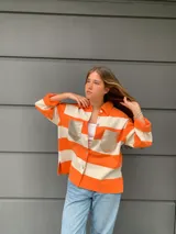 Camisa tejida a rayas horizontales color naranja y blanco, con cuello camisero, mangas tres cuartos y bolsillos frontales con solapa en color dorado.