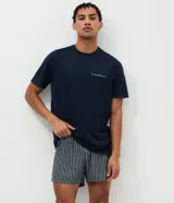 Pijama corto masculino confeccionado en mezcla de algodón, viscosa y elastano. Incluye una remera de manga corta, cuello redondo y bolsillo frontal con detalle listrado, combinada con un short de rayas finas y cintura elástica.
