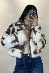 Campera corta de piel sintética con estampado de manchas tipo vaca en tonos blanco y marrón. Presenta cuello camisero, cierre frontal con cremallera y detalles en cuero sintético marrón en el cuello y la solapa del cierre.