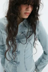 Camisa de denim celeste con cuello solapa, manga larga y cierre frontal con nudos de tela.