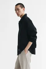 Campera negra de sarga de algodón, con cuello inglés, cierre frontal metálico y bolsillos delanteros ribeteados. Presenta elástico revestido en puños y bajo, y diseño forrado en su interior.