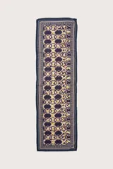 Pareo corto de tejido ligero con estampado geométrico de cadenas en tonos morado, dorado y verde. Presenta un borde con diseño de rayas y puntos.