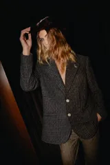 Blazer oversize de diseño asimétrico confeccionado en dos tipos de tweed contrastantes. Presenta solapas clásicas, cierre frontal con botones de strass y un pin decorativo en forma de perro salchicha en la solapa.