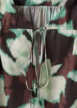 Blusa de gasa con estampado floral en tonos verdes y marrones, cuello escotado con cierre de lazo y mangas largas con puños abotonados.